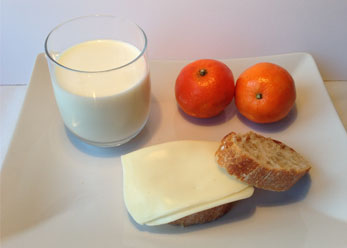 Vaso de leche, pan con queso y mandarinas